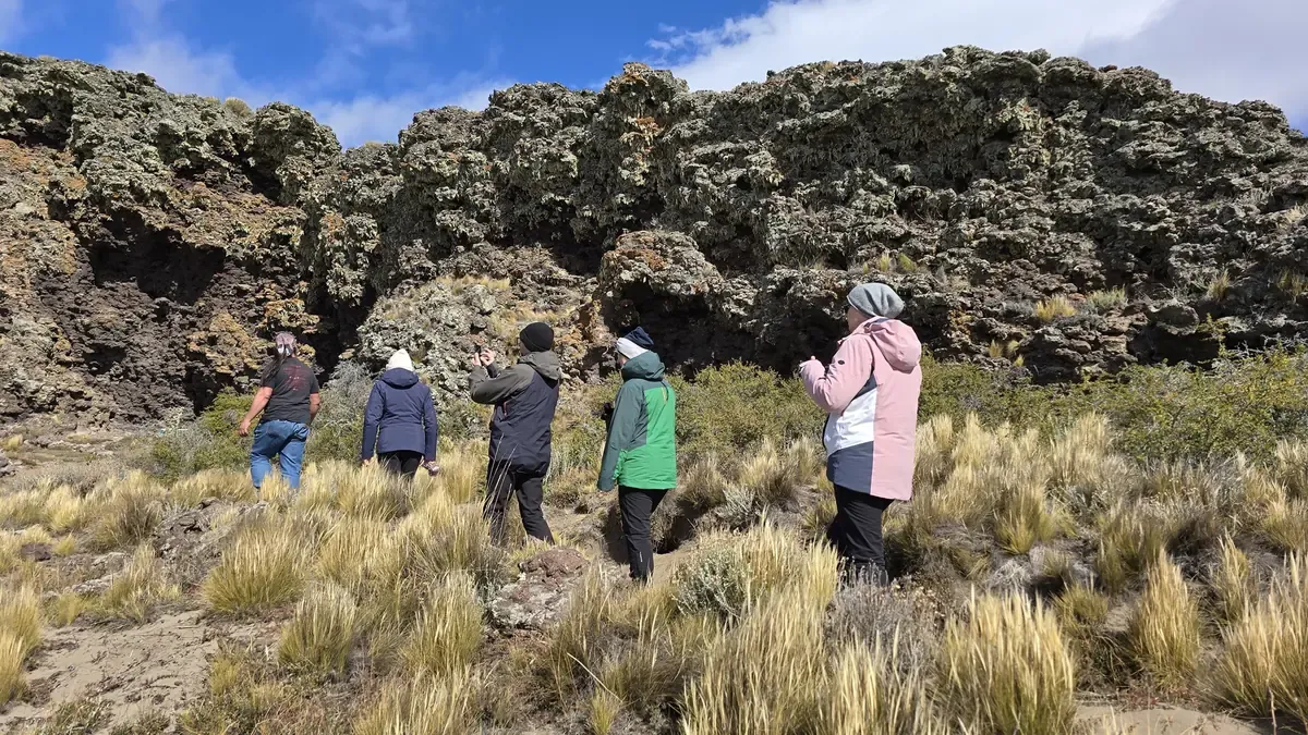 Group walking through tussock grass toward lichen-covered lava walls in Pali Aike.