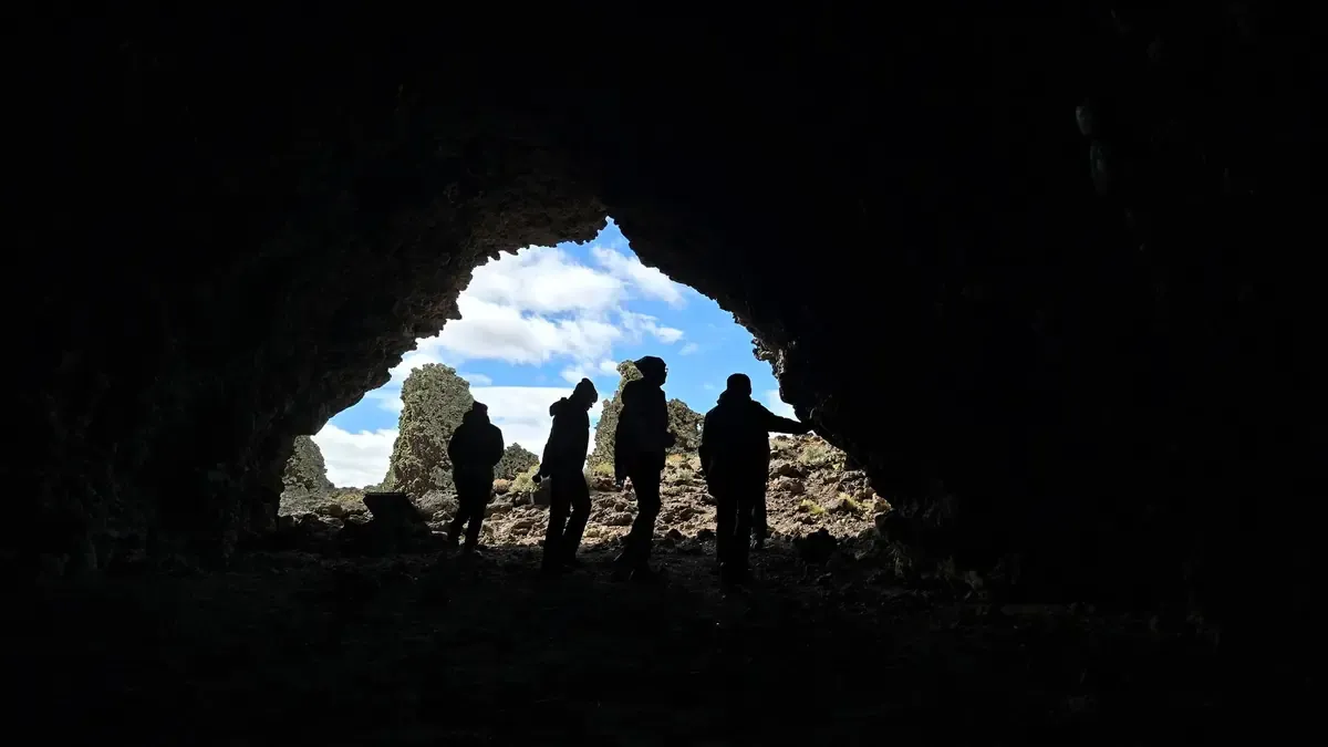 Silhouettes of visitors at the entrance of Pali Aike Cave, with lava formations outside.