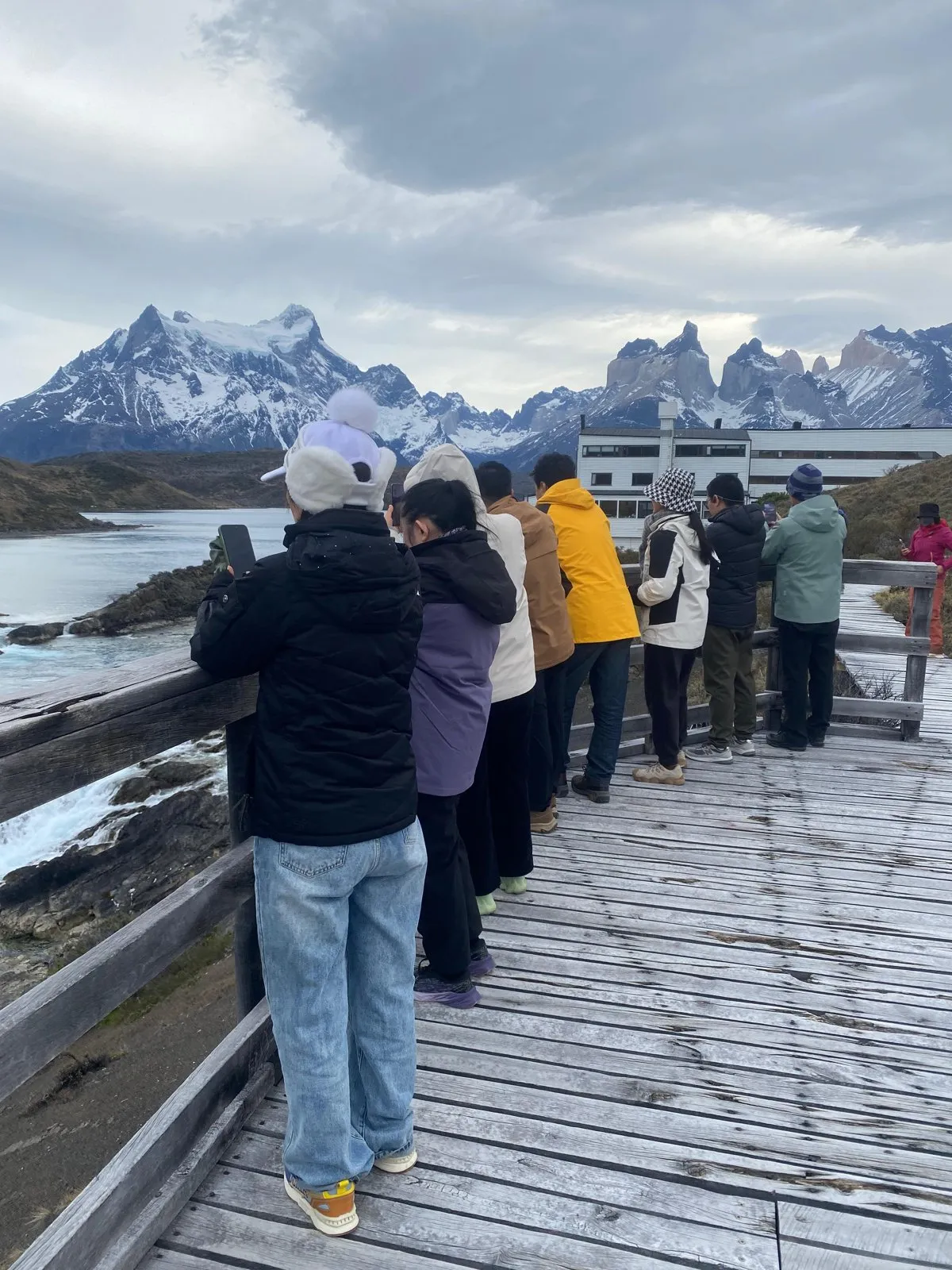 Group of travelers on a boardwalk facing Paine Grande and the Cuernos del Paine