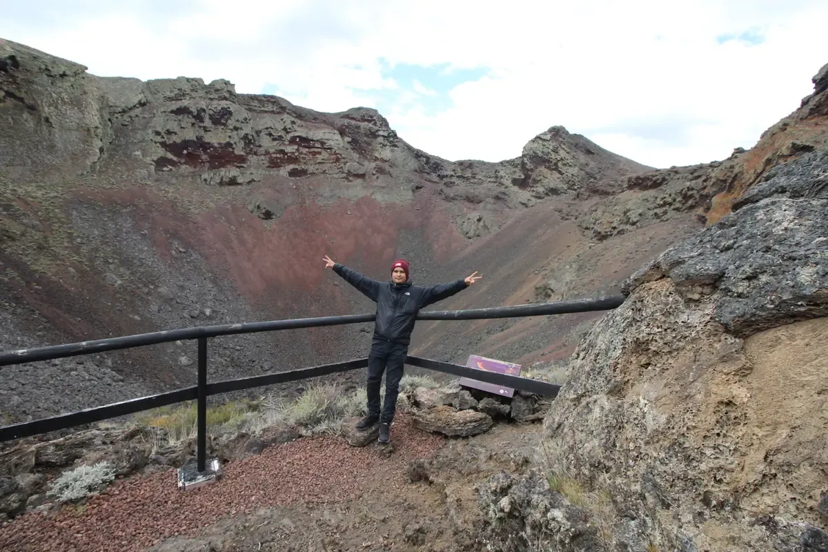 Visitor at the Morada del Diablo crater viewpoint, with reddish volcanic walls behind.