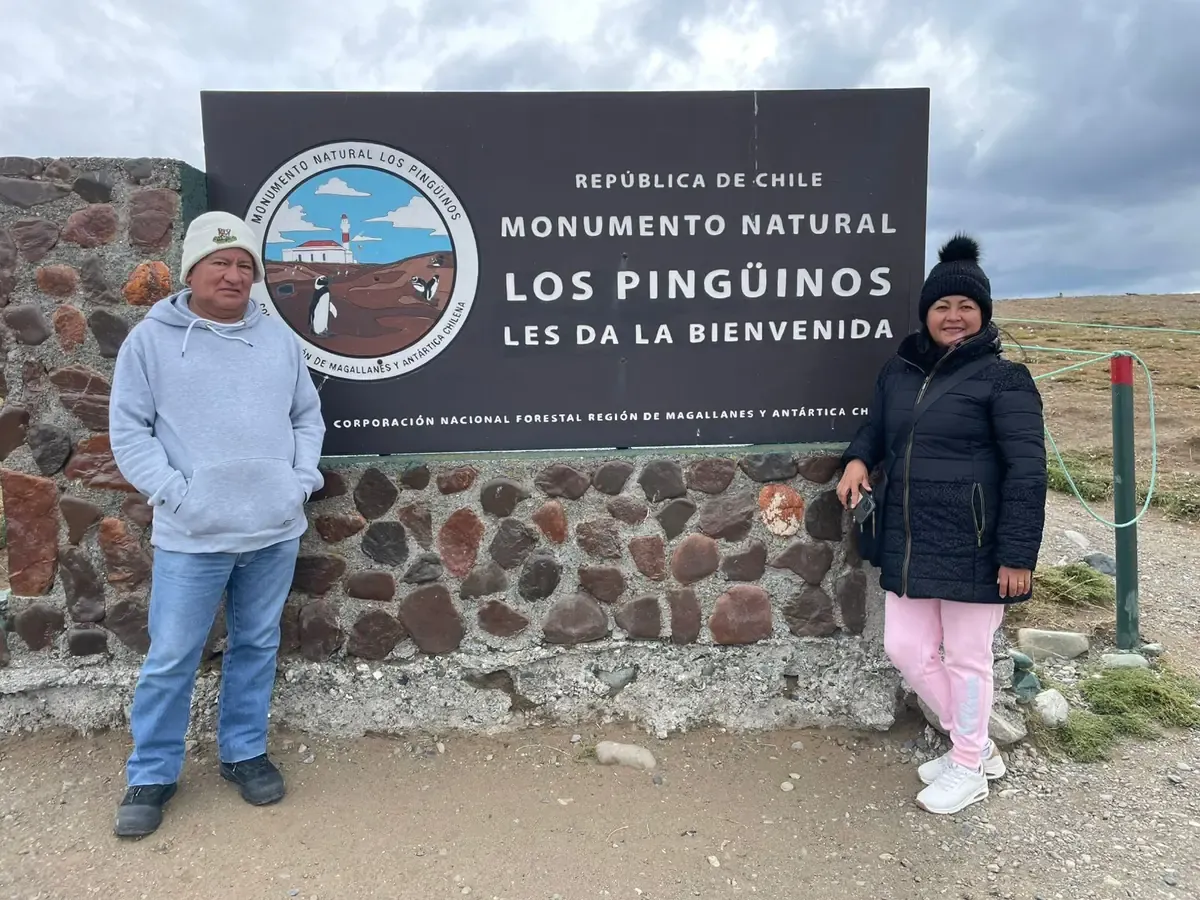 Two visitors beside the Los Pingüinos Natural Monument sign on Magdalena Island