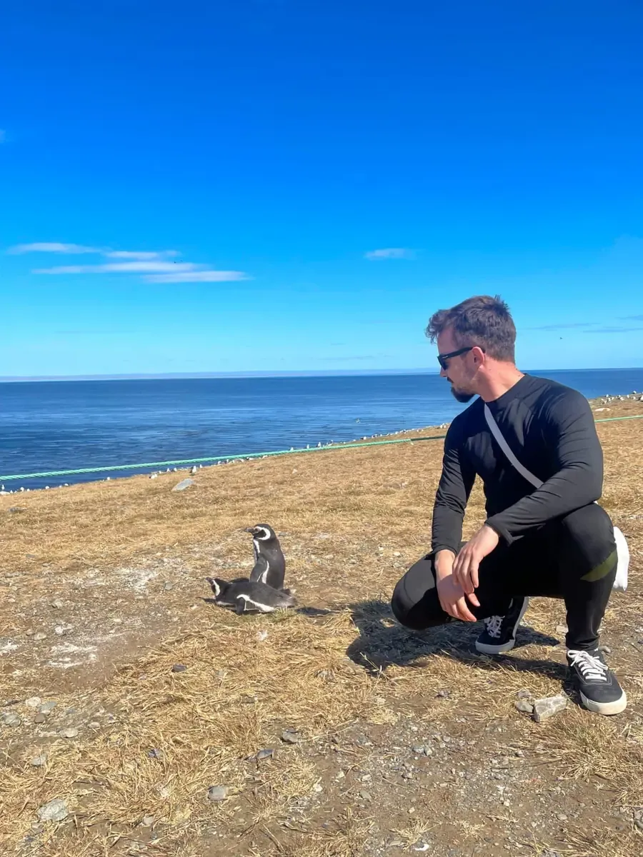 Traveler watching two Magellanic penguins with the sea in the background on Magdalena Island